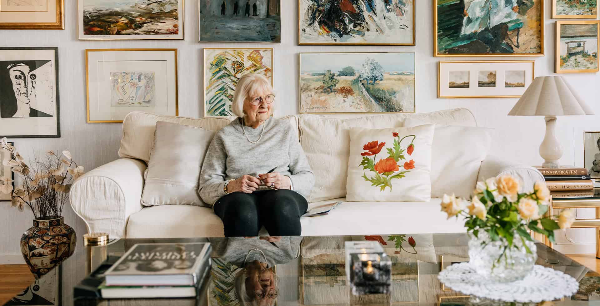 Pia sitter i soffan, på väggen bakom hänger flera tavlor.