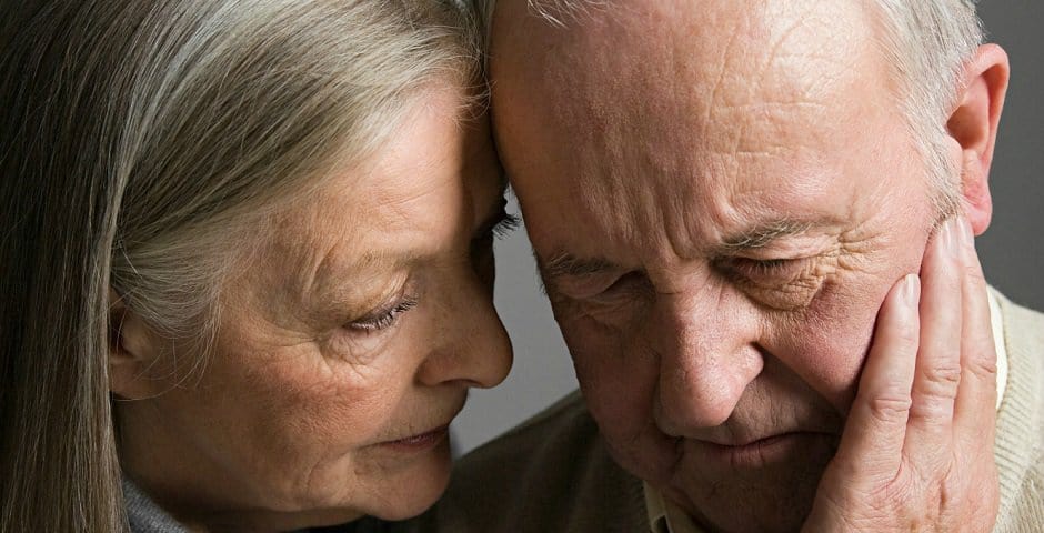 En äldre dam håller handen över kinden på en äldre man.