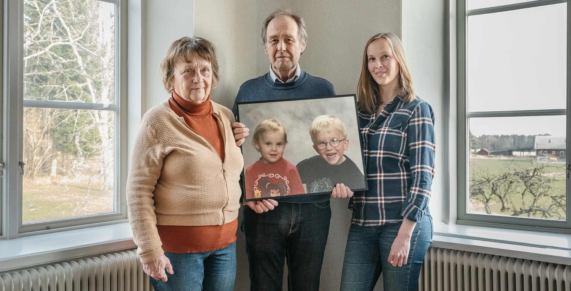 Elin, Ingalill och Anders Löfgren står med ett porträtt av Robert och Elin när de var små.
