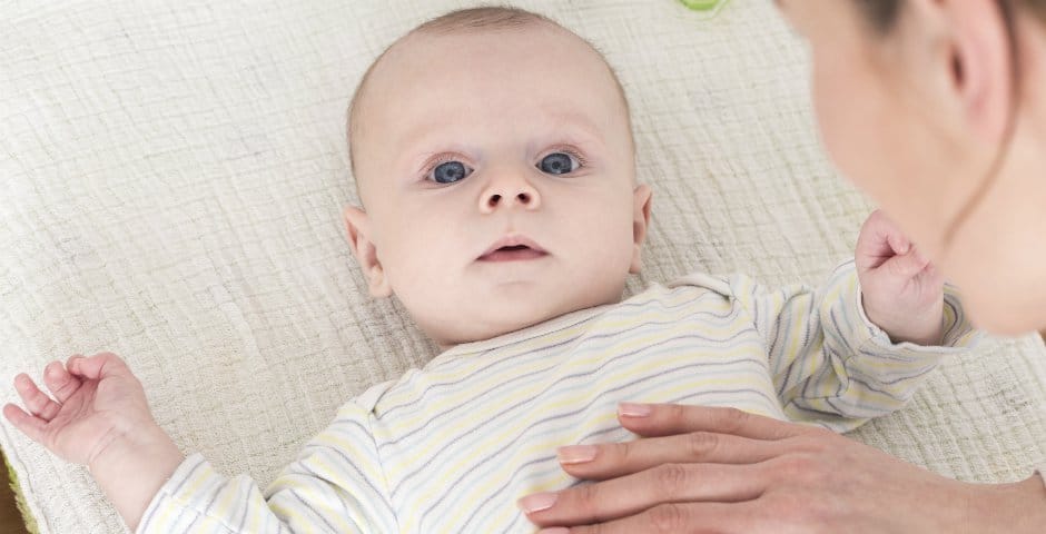 Bebis tittar upp mot kameran och en person som håller sin hand över bebisens mage.