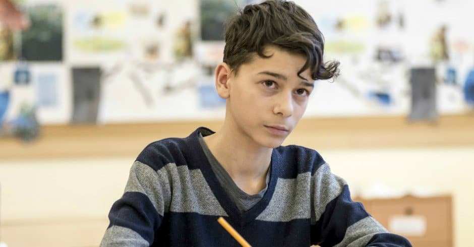 En pojke sitter i ett klassrum med en penna i handen.