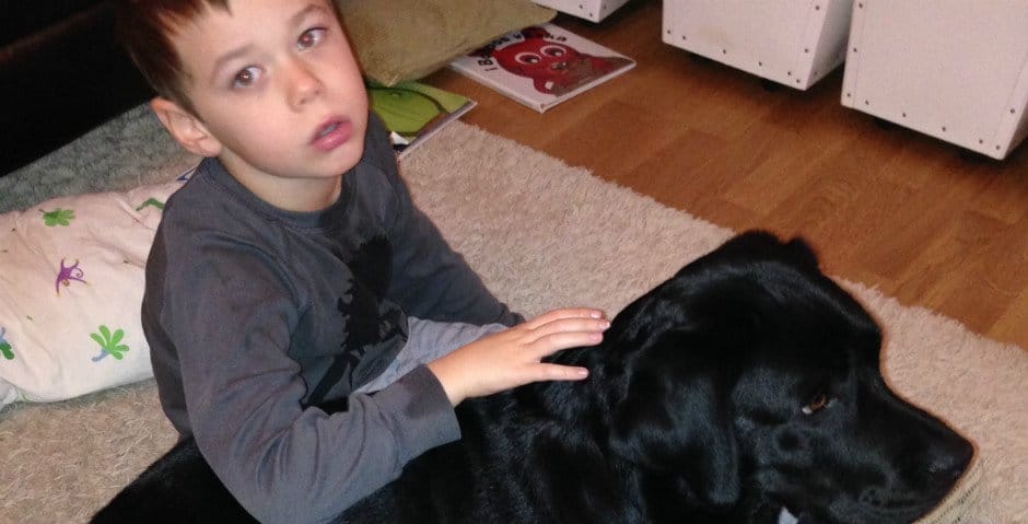Hugo sitter på golvet och klappar på familjens epilepsihund Akira.