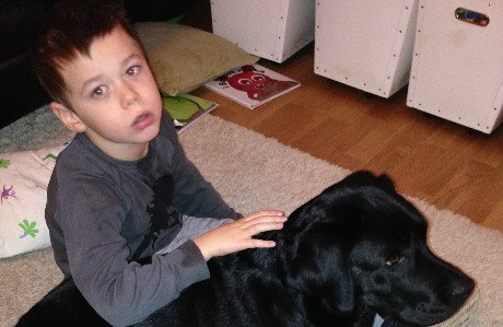 Hugo sitter på golvet och klappar på familjens hund Akira.