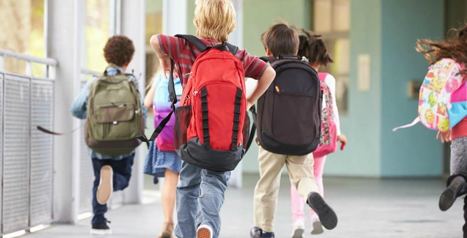 Skolbarn springer med sina skolväskor på ryggen.