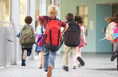 Skolbarn springer med sina skolväskor på ryggen.