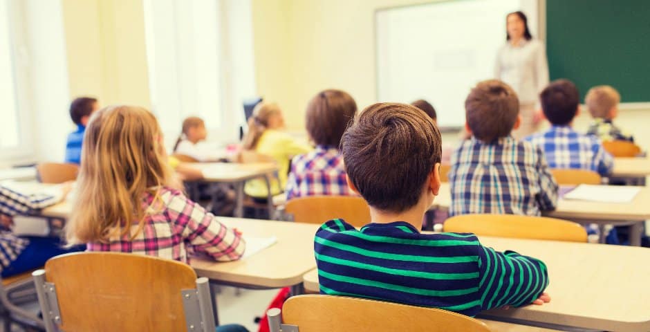 Ett klassrum med barn som sitter vid sina skolbänkar och tittar mot sin lärare.