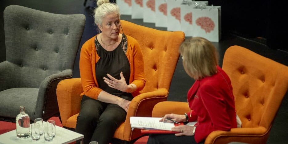 Jessica sitter i en orange stol på scen och samtalar.