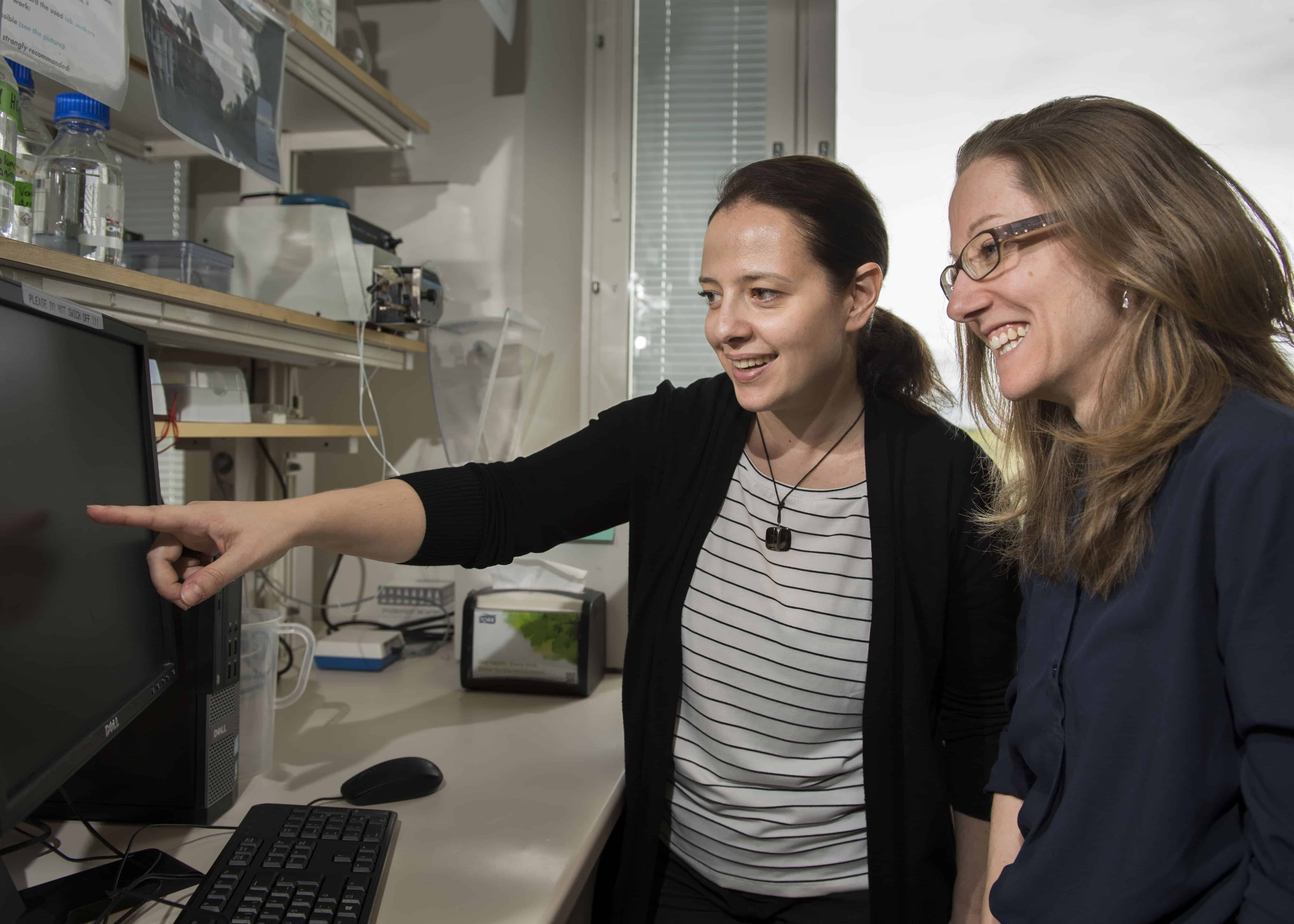 Maja Jagodic och Lara Kular sitter i ett labb och pekar mot en skärm.