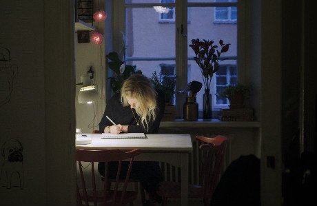 Edith tecknar på ett papper vid ett bord.