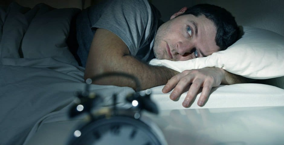 Man ligger med öppna ögon i en säng.
