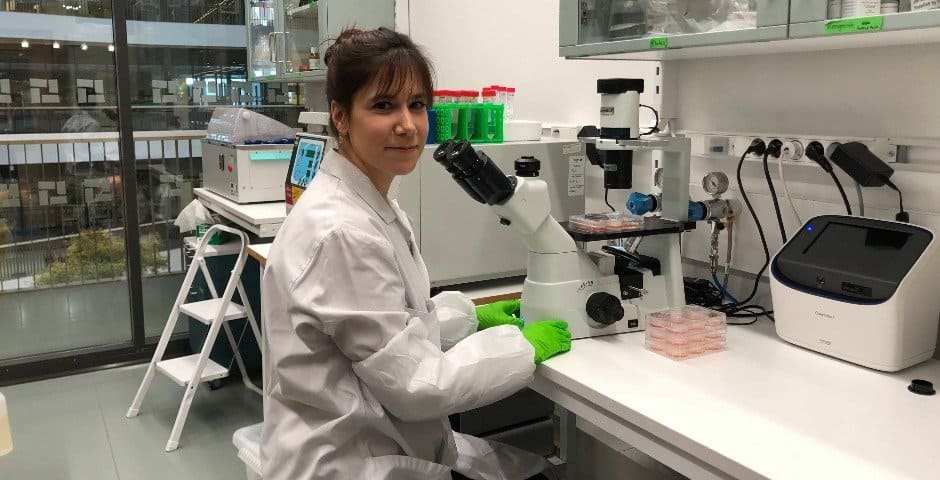 Funda Orhan sitter i ett labb framför ett mikroskop.