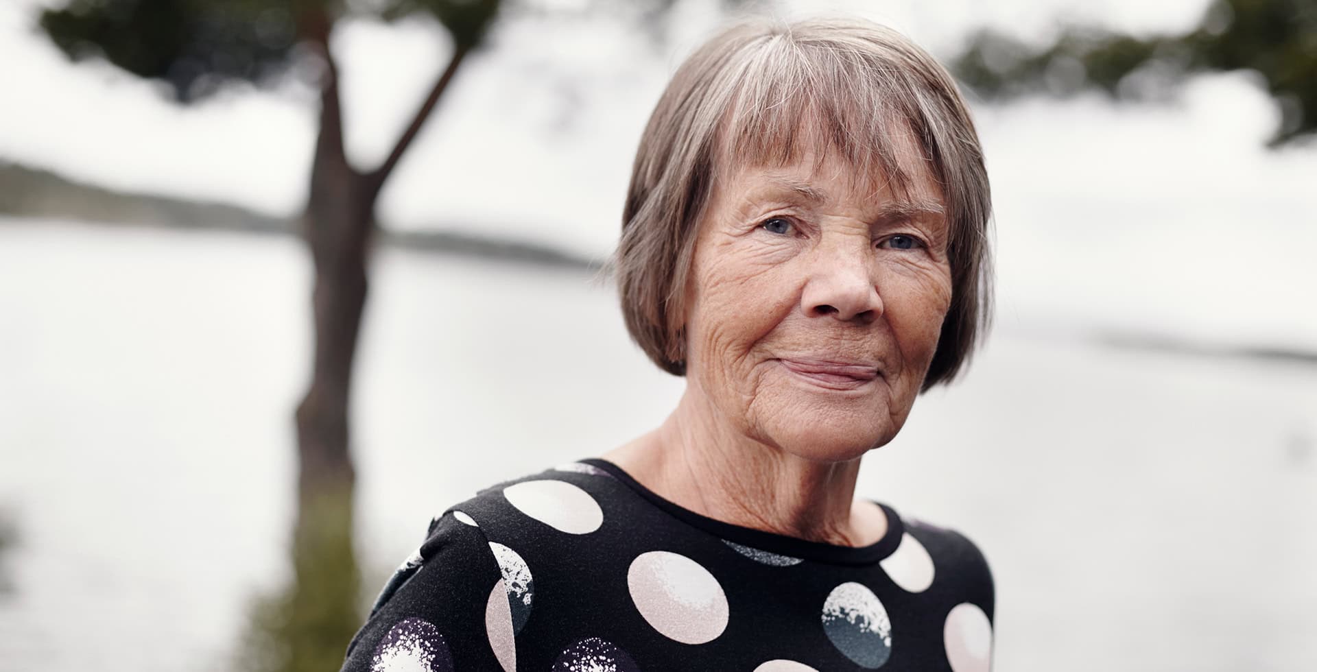 Porträtt av en äldre person som står utomhus vid vatten.