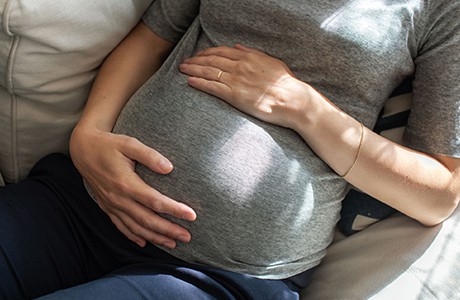 En kvinna håller händer om sin gravidmage.