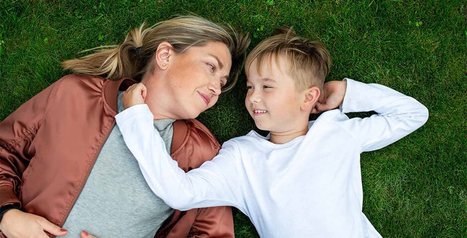 Mamma och pojke ligger i gräset och tittar på varandra.
