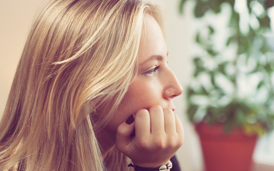 Tonårstjej sitter med hakan i handen och blickar bort.