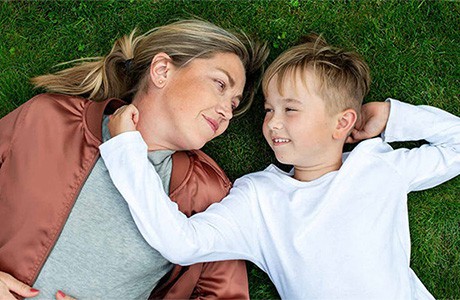 En kvinna och en pojke ligger i gräset och tittar varandra i ögonen.