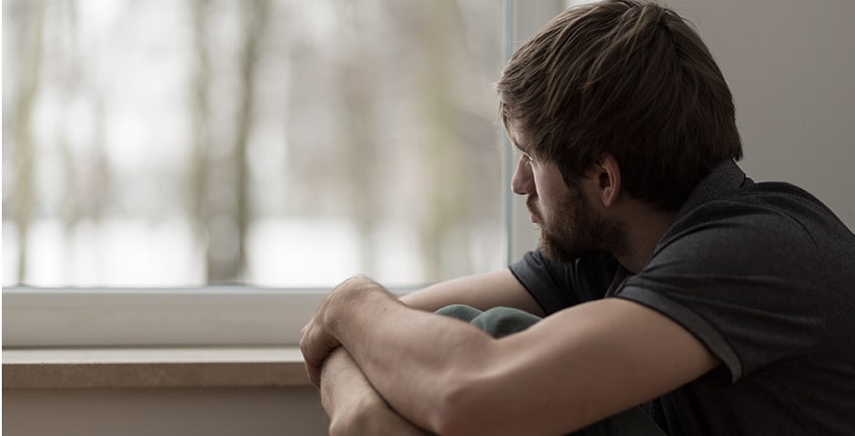 Ung deprimerad man ser ut genom fönstret.