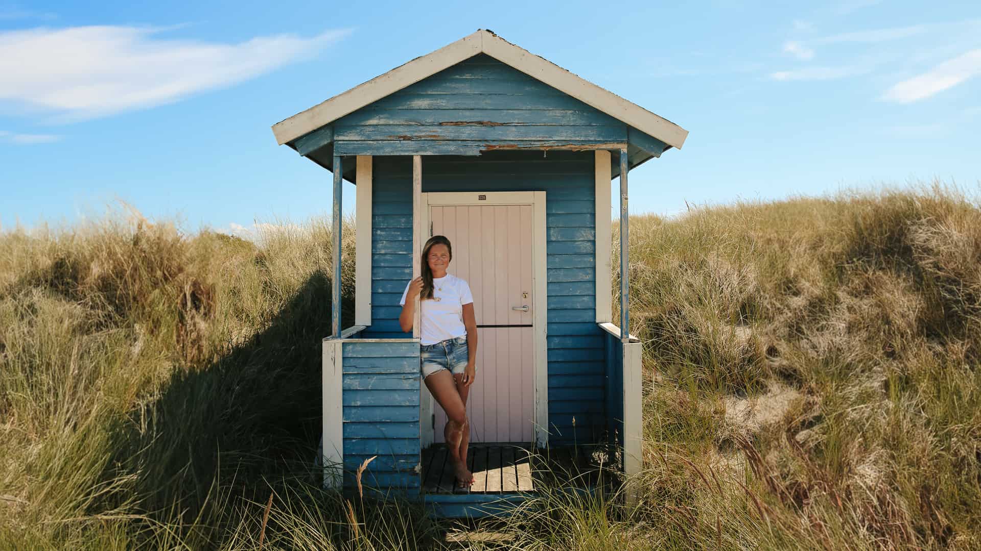 Julia Andrén står vid ett litet blått hus på en strand.