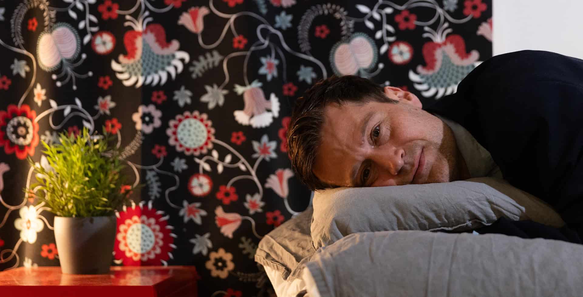 Christian Benedict ligger i en säng och tittar mot kameran.