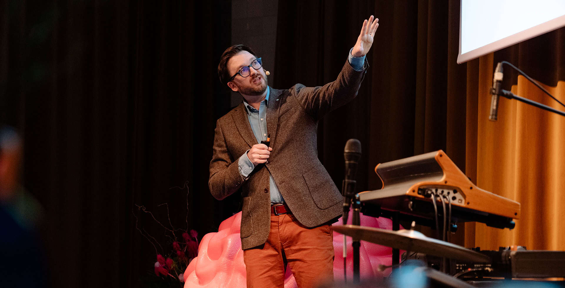 Michael Schöll står på en scen och talar samtidigt som han visar något med händerna.