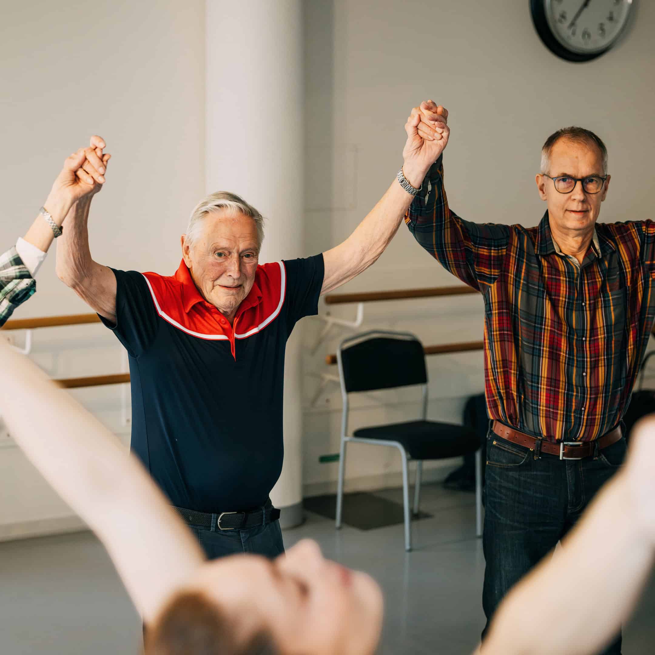 Äldre deltagare håller armarna högt under en gemensam övning i parkinsondans.